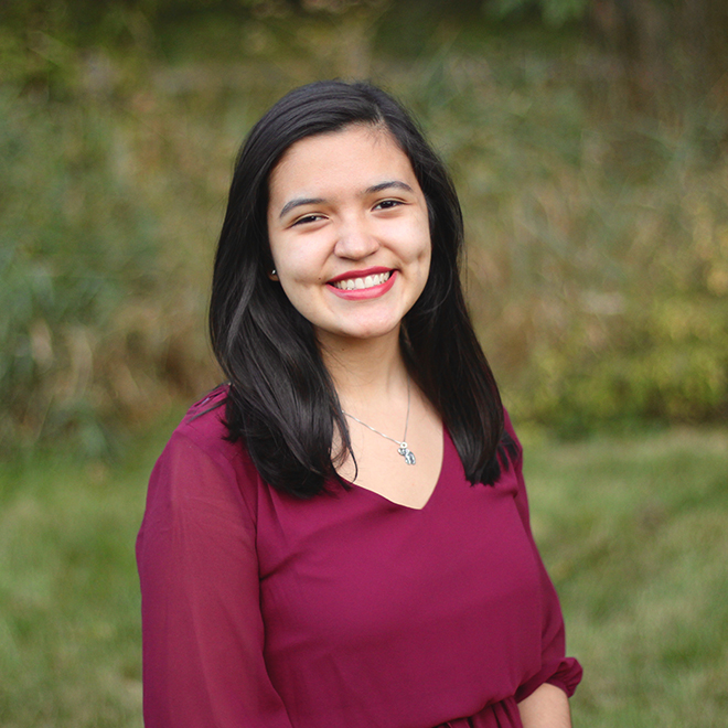 Jackie Guzman, a young woman, smiles at the camera with a green field in the background.