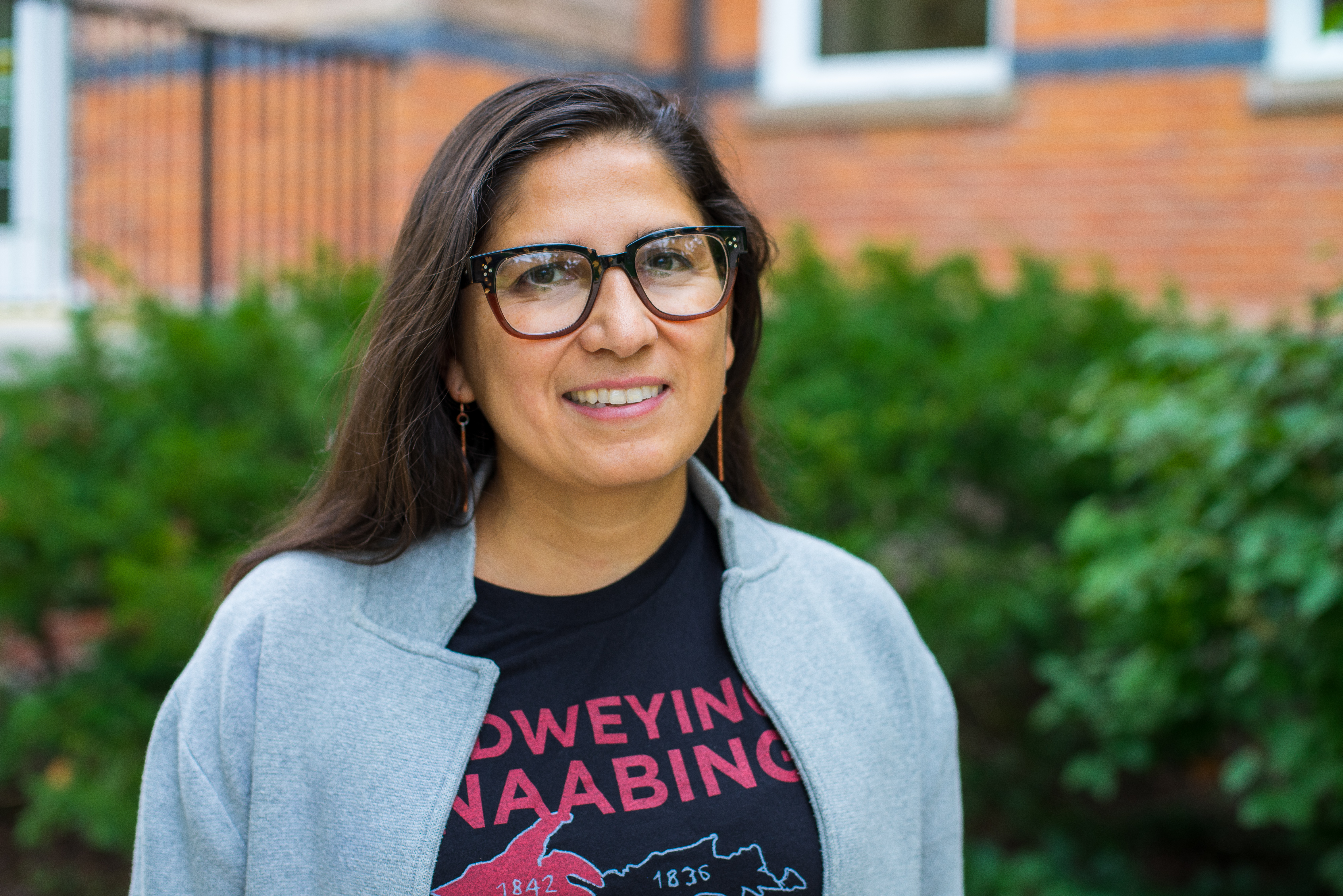 Image shows Professor Estrella Torrez, standing in front of a brick building and smiling.