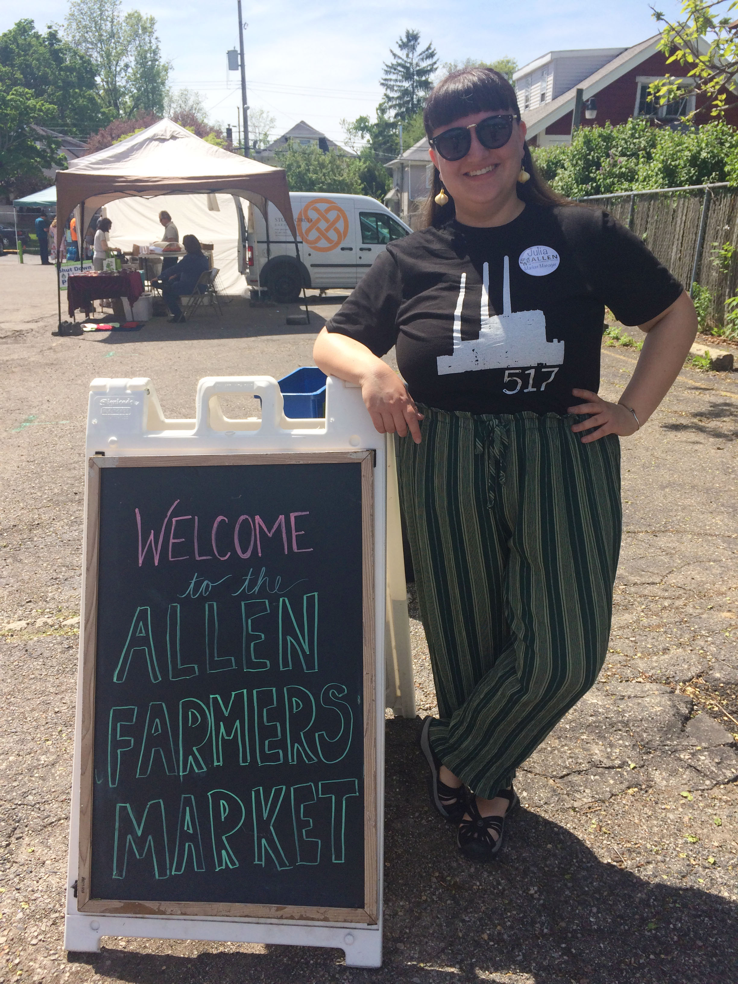 Julia Kramer in sunglasses stands outside in front of a famer's market sign