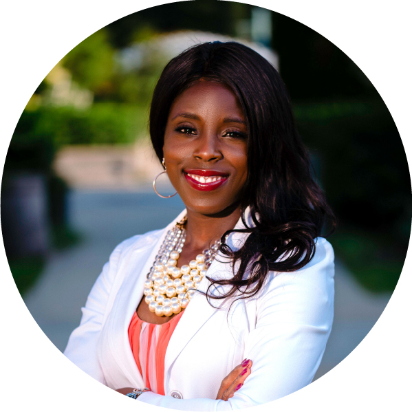 Image shows a Black woman with long hair wearing a white blazer with arms crossed, smiling at the camera.