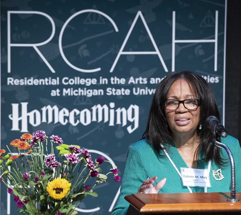 An African American woman with straight black hair, wearing a bright green suit, stands at a podium speaking.